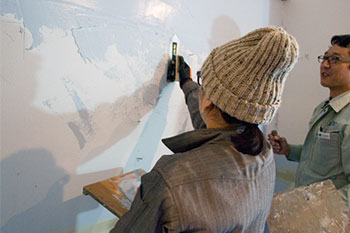 Kさん自ら調合したグレーの塗料を左官職人さんにアドバイスしてもらいながらコテで塗っていく